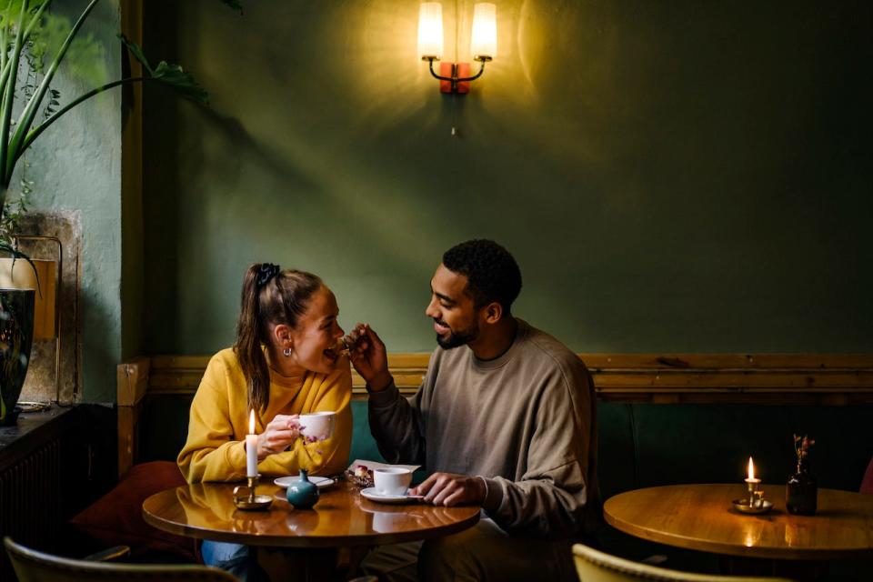 A woman and a man on a date in a dimly lit café, with the man spoon-feeding the woman.