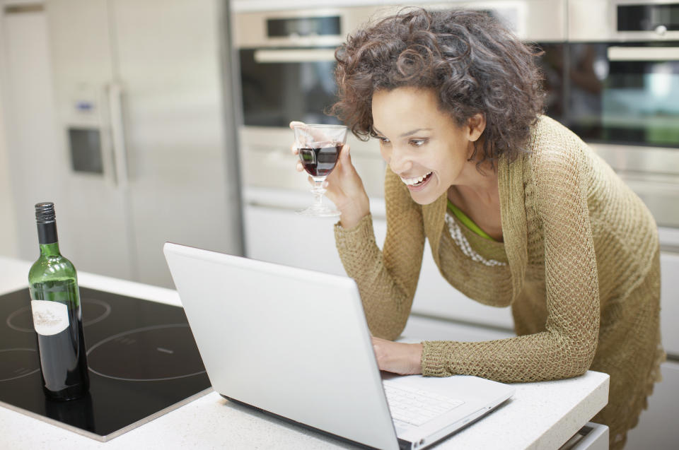 Woman drinking wine and using laptop at home