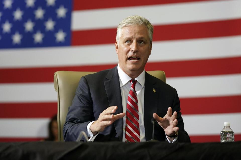 Robert O'Brien gesturing as he speaks from a seat in front of large American flag