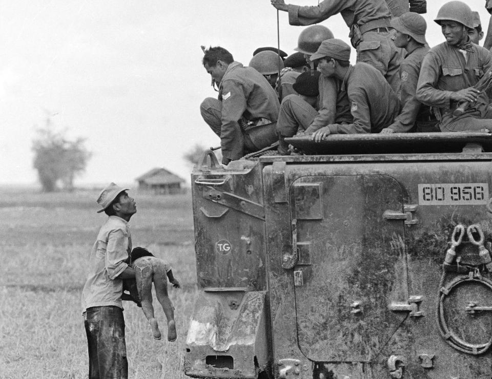 FILE - A father holds the body of his child as South Vietnamese Army Rangers look down from their armored vehicle, March 19, 1964. The child was killed as government forces pursued guerrillas into a village near the Cambodian border. (AP Photo/Horst Faas, File)