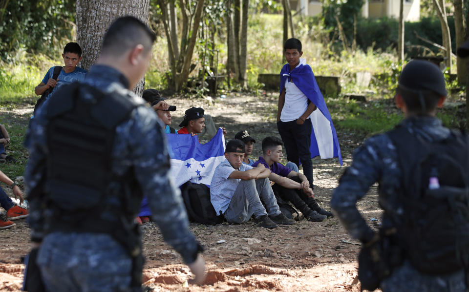 Honduras migrants trying to reach the United States sit with their backpacks and Honduran flags as they are stopped by Guatemalan National Police after crossing the Honduran border, in Morales, Guatemala, Wednesday, Jan. 15, 2020. Migrants in the group said they left Honduras very late Tuesday, around midnight. (AP Photo/Moises Castillo)