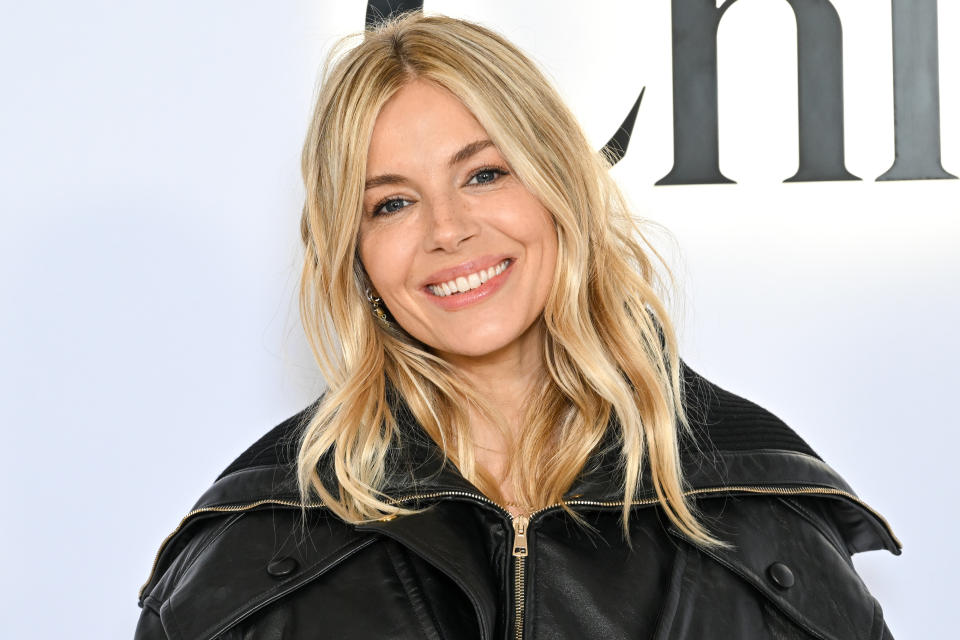 Sienna Miller smiles while wearing a leather jacket at a public event