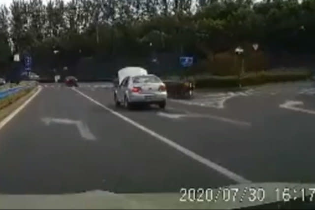 Car moves along Chinese road with bonnet open covering windscreen