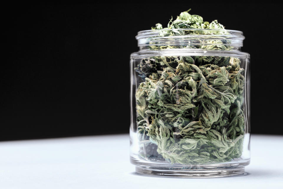 Marijuana leaves in glass jar on table against black background