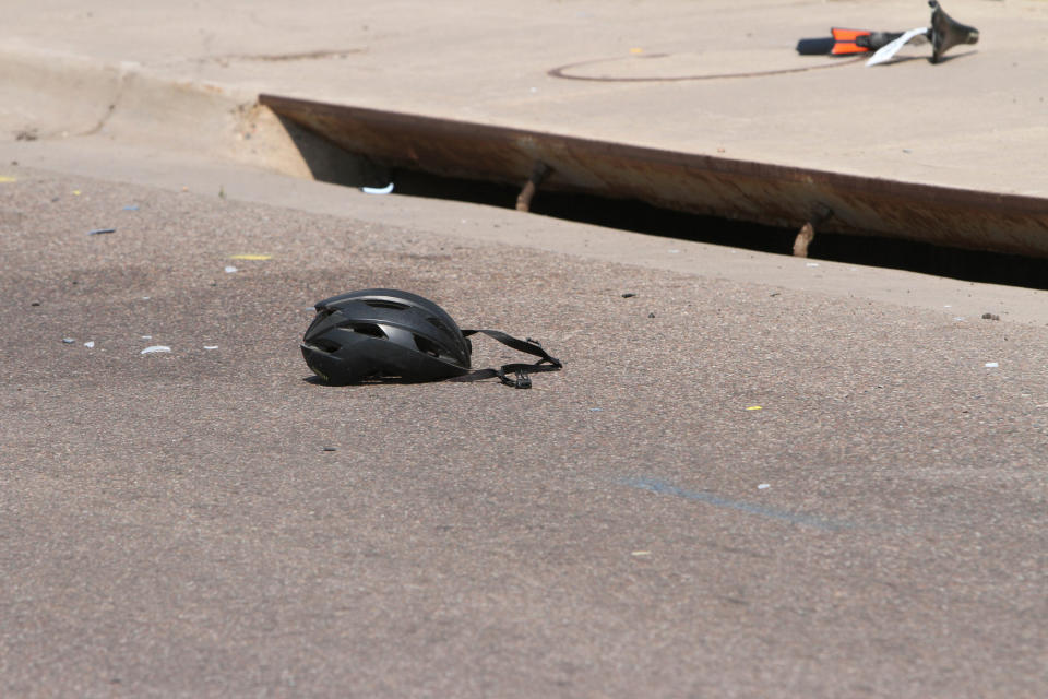 In this Saturday, June 19, 2021, photo courtesy of The White Mountain Independent a cyclist's helmet lies in the road near a damaged bike in Show Low, Ariz. A driver in a pickup truck plowed into bicyclists competing in a community road race in Arizona on Saturday, critically injuring several riders before police chased down the driver and shot him outside a nearby hardware store, police said. (Jim Headley/The White Mountain Independent via AP)