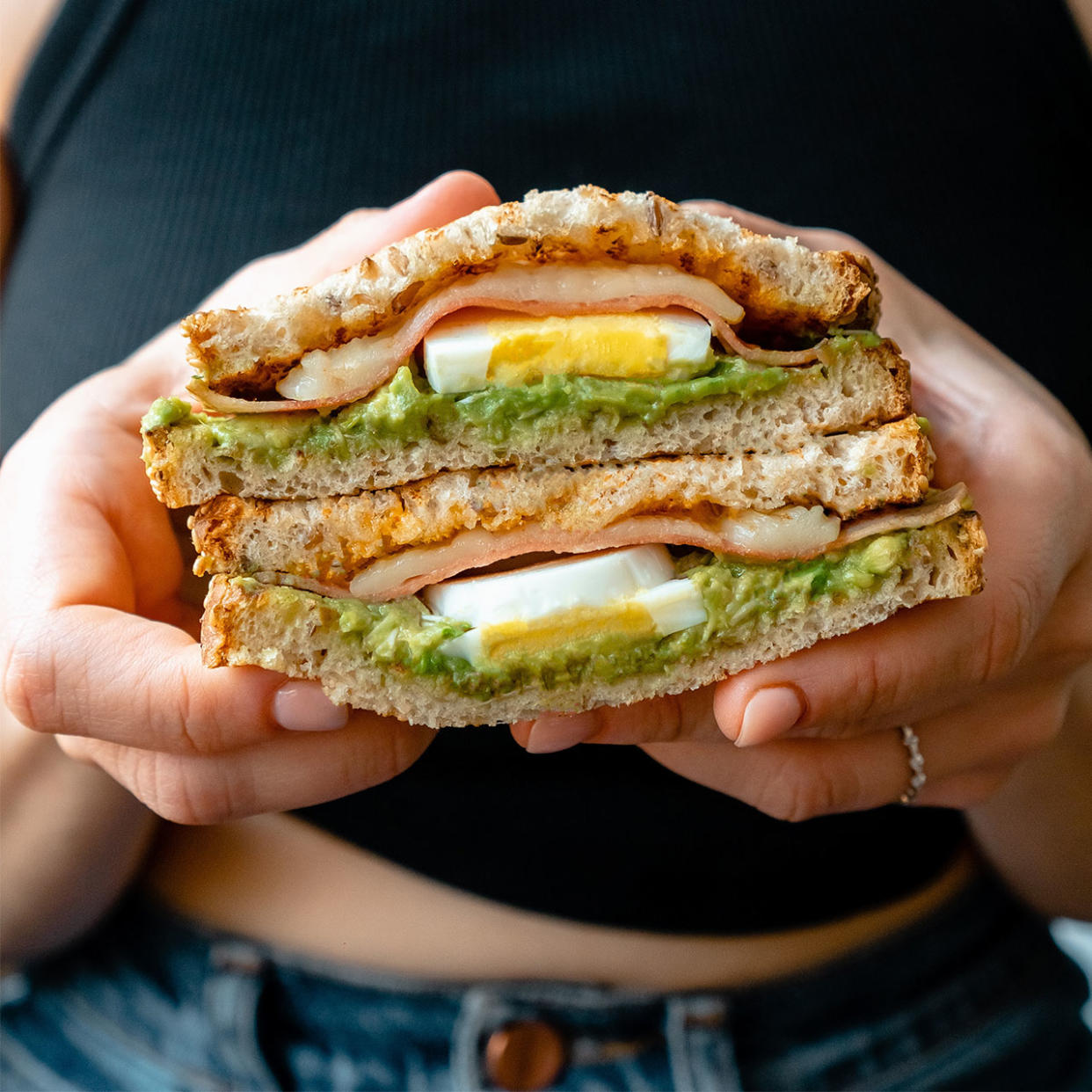 woman holding up a breakfast sanwich with avocados and eggs