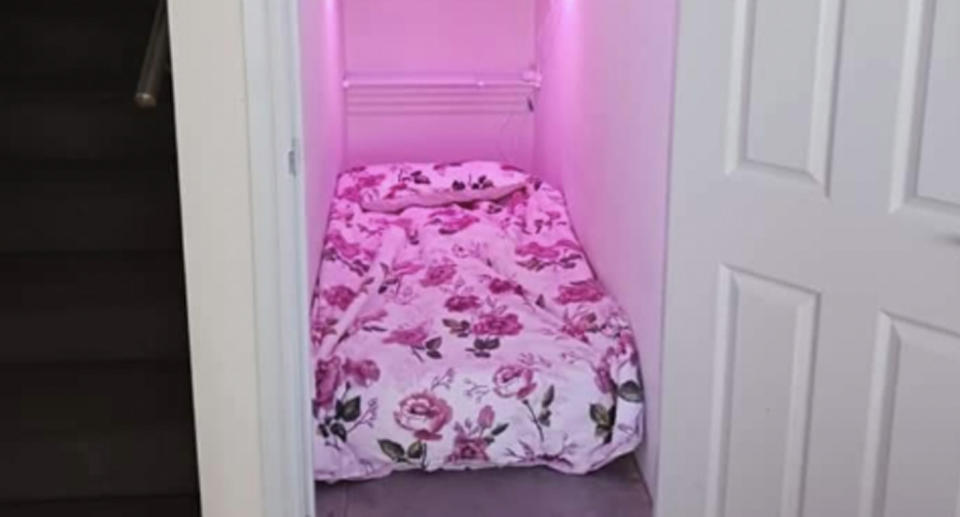 The 'pantry room' can be seen with a single bed squashed into the space, with fluorescent pink lights hanging overhead beside a dark staircase outside. 