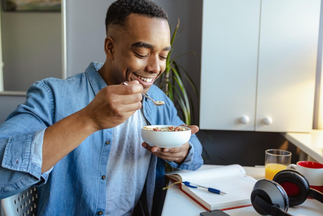 Young man home eating breakfast and working on the laptop