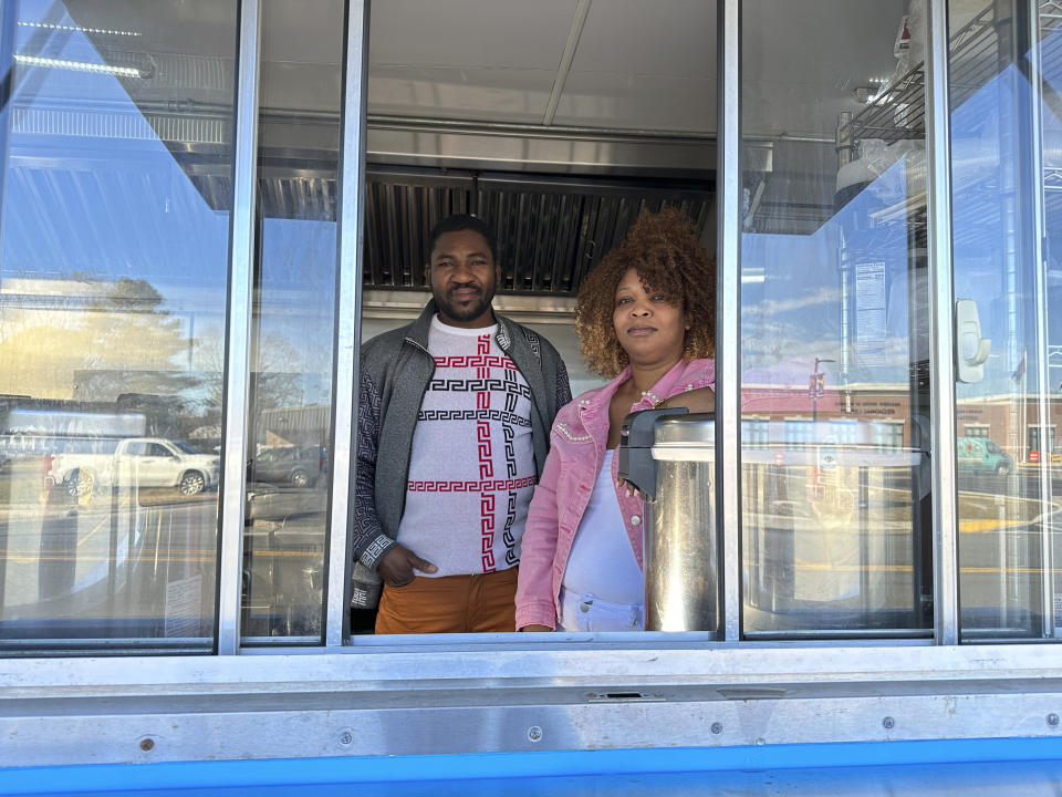 Theslet Benoir and Clemene Bastien stand at the window of their Eben-Ezer Haitian food truck in Parksley, Va., on Wednesday, Jan. 24, 2024. The married couple is suing the town in federal court over allegations that their food truck was forced to close. The couple also says a town councilman cut the mobile kitchen's water line and screamed, "Go back to your own country!" (AP Photo/Ben Finley)