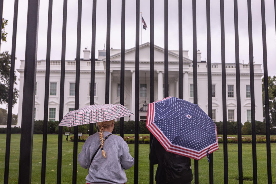 Two people stand in front of the White House on Saturday, holding umbrellas.