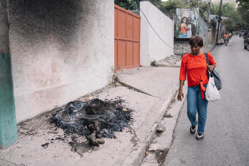 <br>A woman avoids the smoldering remains of an alleged gang member who was lynched by Bwa Kale vigilantes.