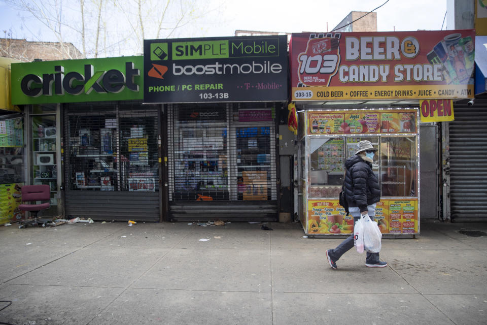 A woman wears a face masks to protect against the coronavirus as she carries her groceries past closed shops on Roosevelt Avenue, Tuesday, April 14, 2020, in Corona neighborhood of the Queens borough of New York. (AP Photo/Mary Altaffer)