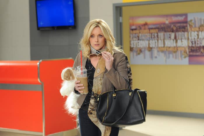 Jenna Maroney walks into a studio holding a huge coffee and a tiny dog