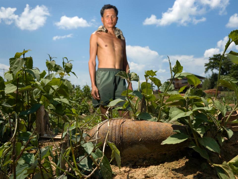 A farmer stands beside a live mortar he found on his land in Laos.