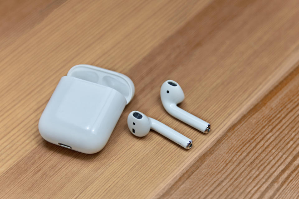Mobile airpods on wooden blurred background. Apple wireless earphones with charger box, chosen focus. Indoors, copy space, close up.