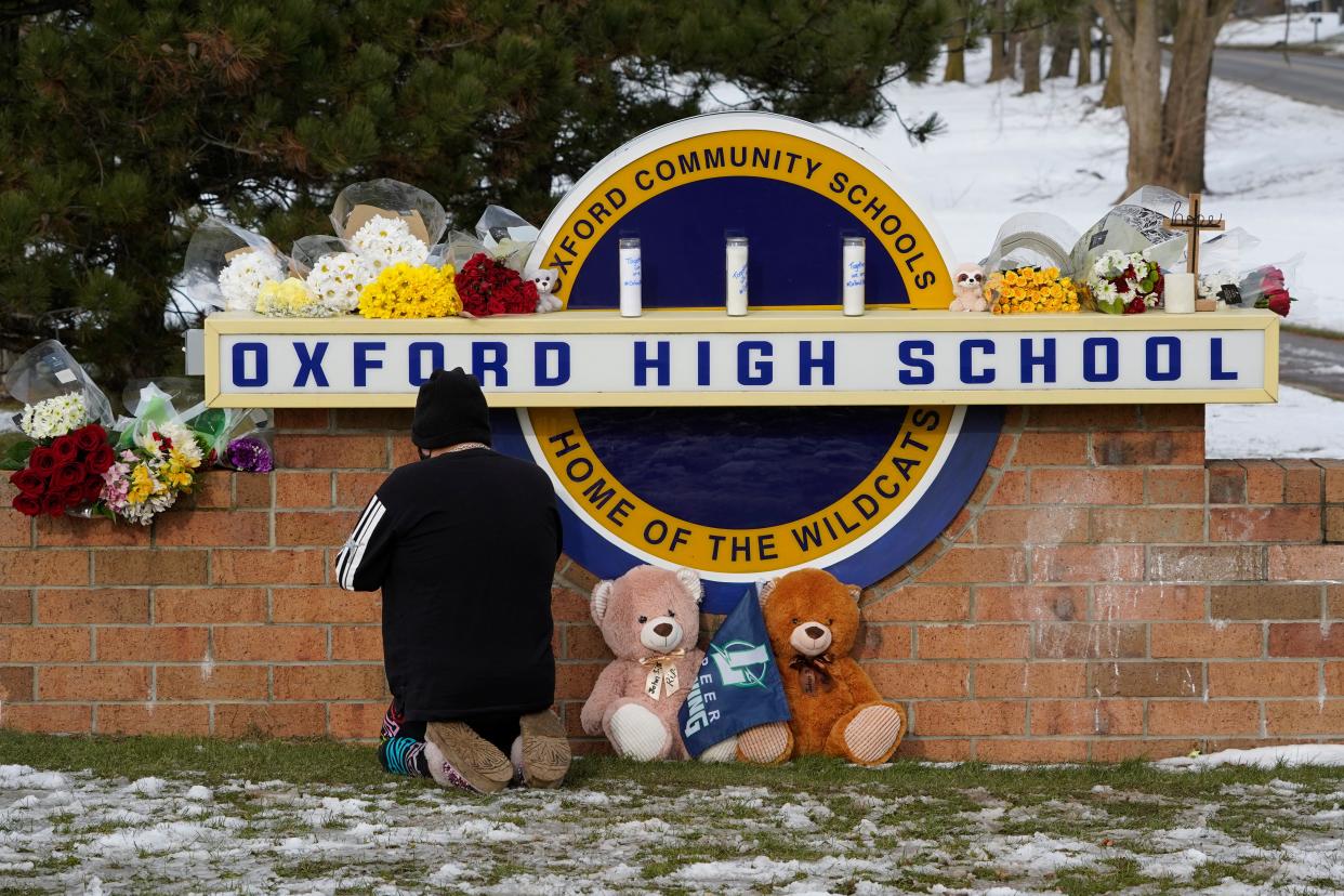 A well wisher kneels to pray at a memorial on the sign of Oxford High School in Oxford, Mich., Wednesday, Dec. 1, 2021. A 15-year-old sophomore opened fire at the school, killing several students and wounding multiple other people, including a teacher. (AP Photo/Paul Sancya)