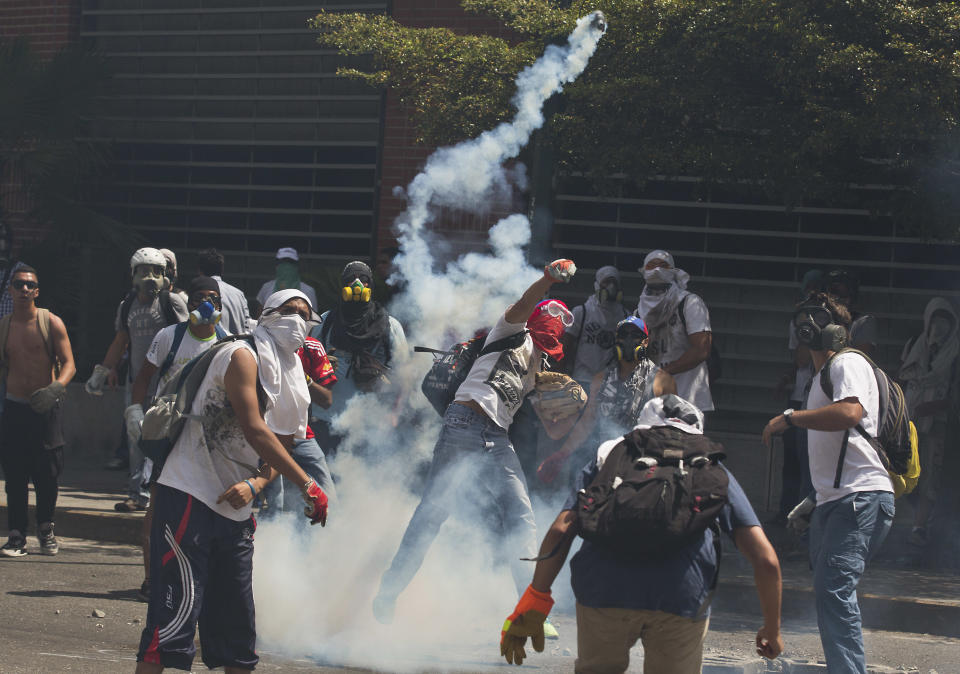 Anti-government demonstrators wearing masks, throw back tear gas canisters fired by Bolivarian National Police during clashes at the Central University of Venezuela, UCV, in Caracas, Venezuela, Thursday, March 20, 2014. Thursday dawned with two more opposition politicians, San Cristobal Mayor Daniel Ceballos and San Diego Mayor Enzo Scarano, behind bars. Police used tear gas and water cannons to disperse a student-called protest of several thousand people in Caracas, some of those demonstrating against the arrests of the mayors. (AP Photo/Esteban Felix)