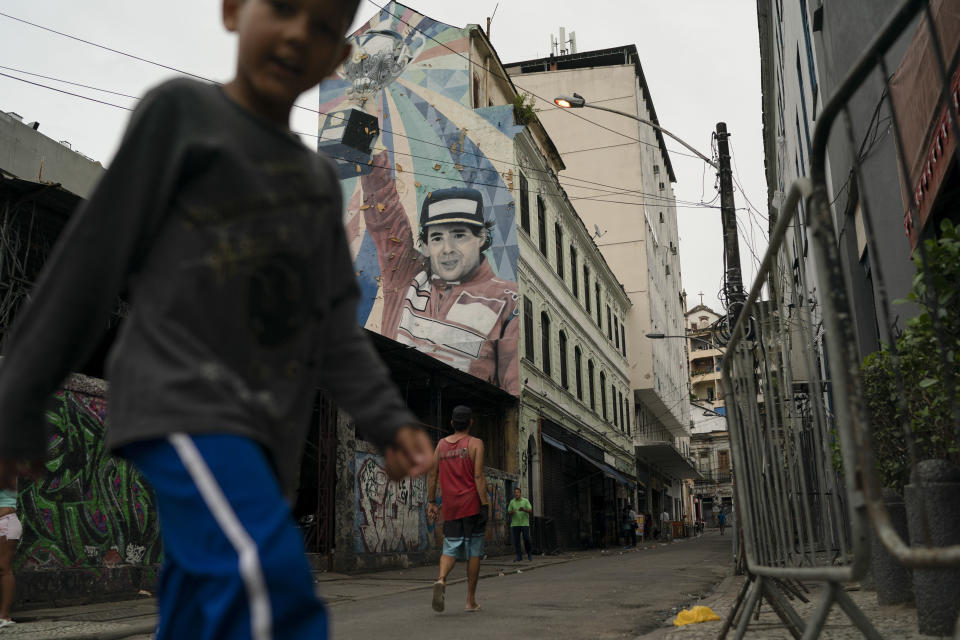 In this Nov. 7, 2019 photo, people walk past a building decorated with mural art depicting legendary Brazilian F1 driver Ayrton Senna, in Rio de Janeiro, Brazil. Rio has the exuberance of samba and Carnival, plus dramatic postcard views of beaches and verdant mountains. Now, to Sao Paulo's chagrin, Rio is pushing for an F1 racetrack, too. (AP Photo/Leo Correa)