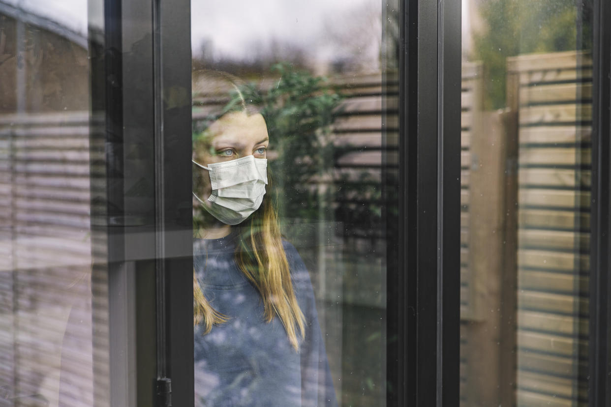 Teenage girl looking through window with mask
