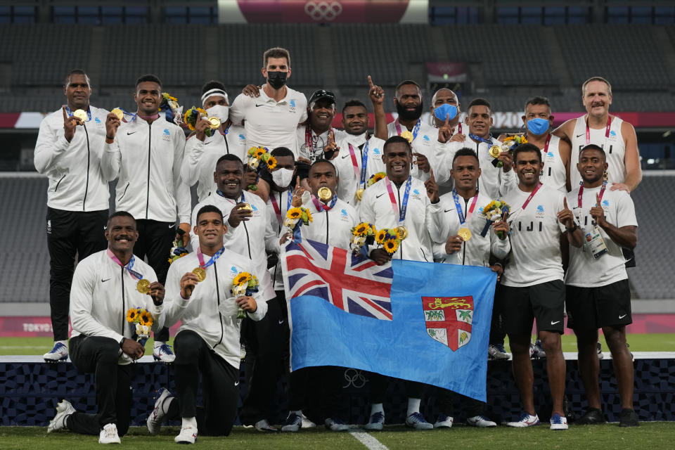 Fiji players and team staff poses with their gold medals and a national flag, after winning men's rugby sevens at the 2020 Summer Olympics, Wednesday, July 28, 2021 in Tokyo, Japan. (AP Photo/Shuji Kajiyama)