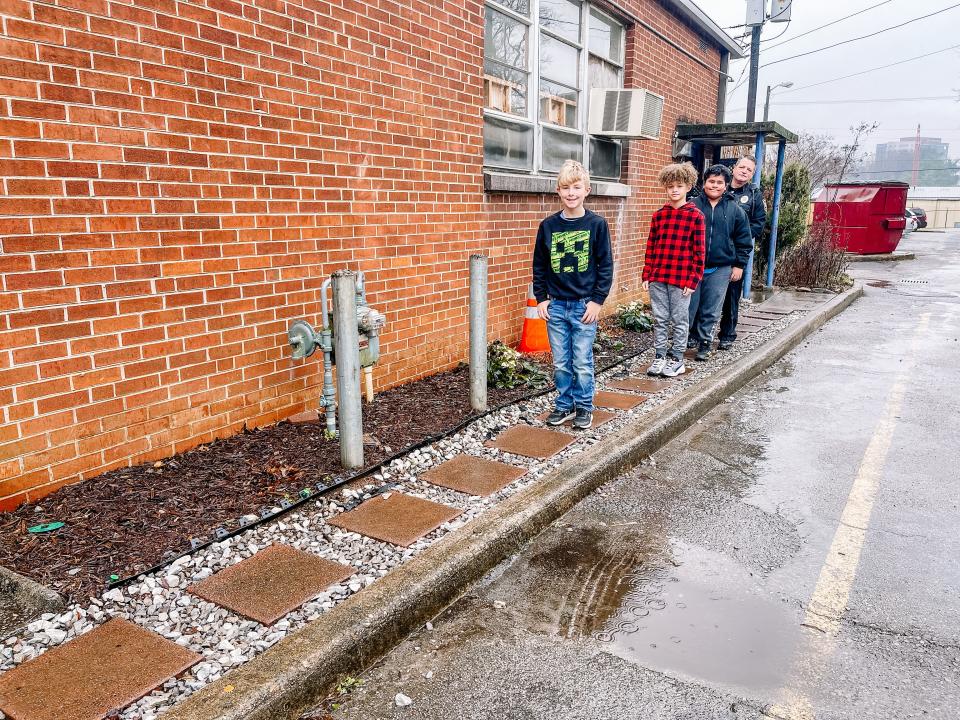 School Resource Officer Doug Grimm shows off the Iron Man Club’s service project with Joseph Jordan, front, Ethan Gonzalez and Christian Crenshaw at South Knoxville Elementary. The club spent many weeks putting in a French drain, adding paving stones so that students wouldn’t have to walk through a big mud pit to get to their car. Feb. 3, 2022.