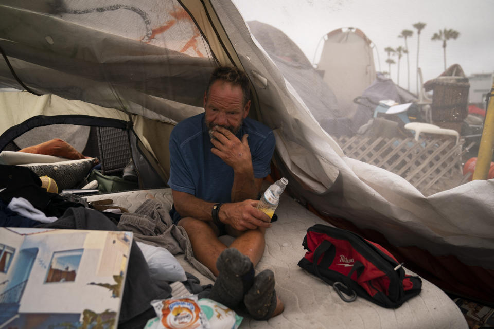 FILE - In this June 29, 2021, file photo, Scott See passes time in his tent at a homeless encampment set up along the boardwalk in the Venice neighborhood of Los Angeles. The recall election that once threatened Gov. Gavin Newsom's political career has instead given it new life, The rare midterm vote of confidence could fuel an ambitious legislative agenda featuring new coronavirus vaccine mandates, housing for the homeless and health insurance for people living in the country illegally. (AP Photo/Jae C. Hong, File)