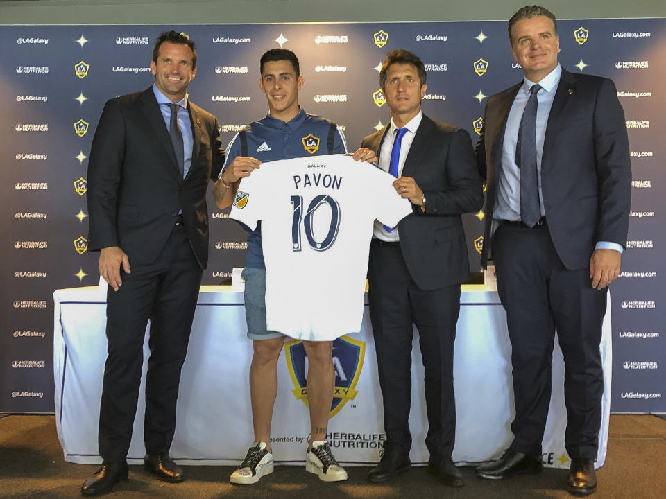 Forward Cristian Pavón, second from left, of Argentina, holds up his new LA Galaxy jersey at Dignity Health Sports Park in Carson, Calif., Thursday, Aug. 8, 2019. Standing alongside Pavon, Galaxy President Chris Klein, left, head coach Guillermo Barros Schelotto, second from right, and general manager Dennis te Kloese. The LA Galaxy acquired Pavón on loan from Argentina's Boca Juniors this week in one of the biggest player acquisitions in recent Major League Soccer history. (AP Photo/Greg Beacham)