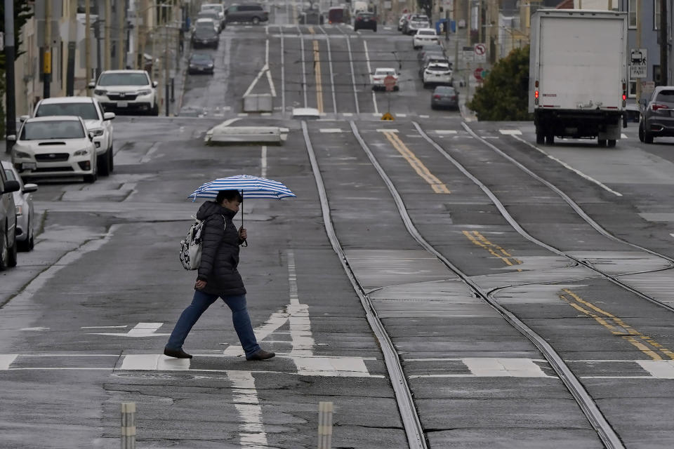 FILE - A pedestrian carries an umbrella while crossing a street in San Francisco, Thursday, April 14, 2022. A variety of new laws take effect Sunday, Jan. 1, 2023 that could have an impact on people's finances and, in some cases, their personal liberties. (AP Photo/Jeff Chiu, File)