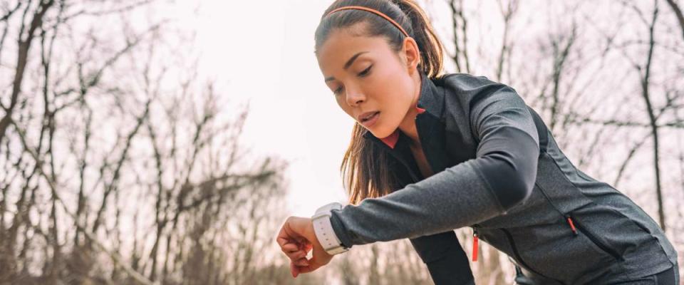 woman running on a trail, looking at smart watch, bent over