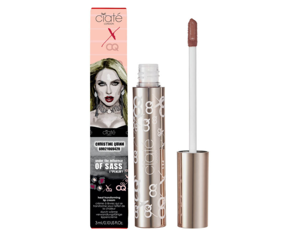 The package for Ciate London's colour-changing lip cream, with an image of Christine Quinn, stands upright on the left with the gold tube open in the middle with the applicator on the right against a white background.
