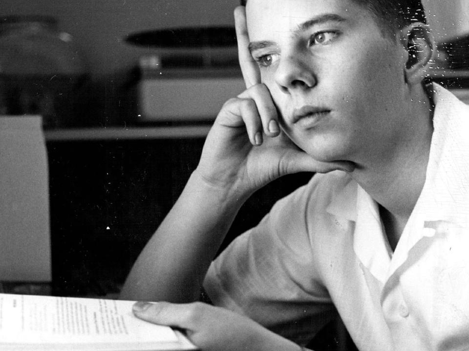 A young boy thinking with one hand supporting his head and the other holding a book.