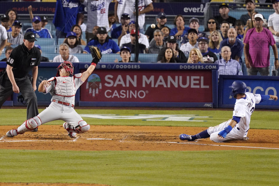 Los Angeles Dodgers' Chris Taylor, right, scores on a single by Zach McKinstry as Philadelphia Phillies catcher J.T. Realmuto, center, misses the ball while home plate umpire Ryan Wills watches during the fourth inning of a baseball game Tuesday, June 15, 2021, in Los Angeles. (AP Photo/Mark J. Terrill)