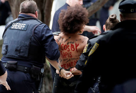 A protester is escorted out by the the police after breaking through the barriers, as actor and comedian Bill Cosby arrives for the first day of his sexual assault retrial at the Montgomery County Courthouse in Norristown, Pennsylvania, U.S., April 9, 2018. REUTERS/Jessica Kourkounis