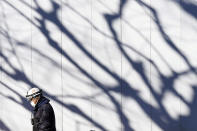 A construction worker wearing a protective mask walks by a wall where shadow of tree cast Wednesday, Dec. 29, 2021, in Tokyo. Caseloads of omicron have remained relatively low in many countries in Asia. For now, many remain insulated from the worst, although the next few months will remain critical. (AP Photo/Eugene Hoshiko)