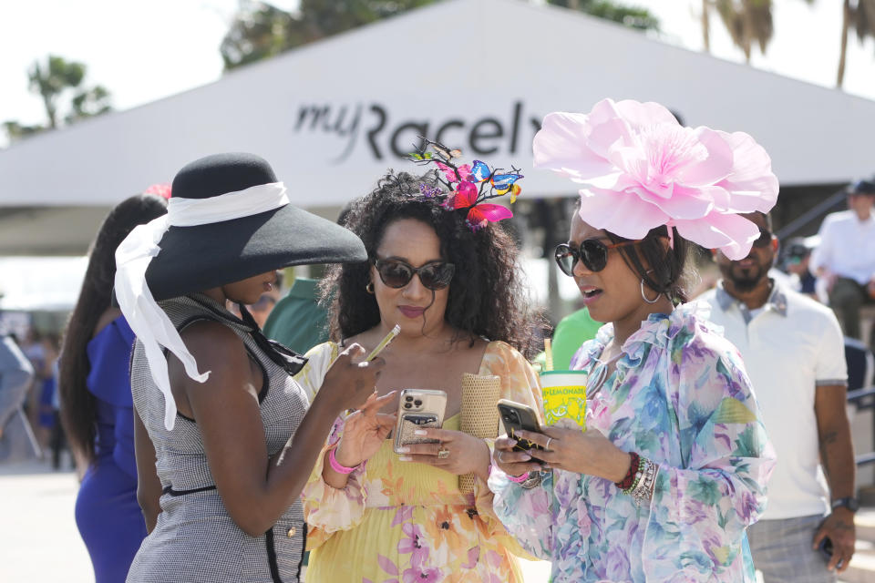 Daveeka Burns, left, Nefertiti Thomas, center, and Dr. Tanda Mercer look at their phones between races at the Pegasus World Cup day horse races, Saturday, Jan. 27, 2024, at Gulfstream Park in Hallandale Beach, Fla. (AP Photo/Wilfredo Lee)