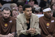San Antonio Spurs center Victor Wembanyama, center, sits on the bench with an ankle injury during the second half of an NBA basketball game against the Phoenix Suns in San Antonio, Monday, March 25, 2024. (AP Photo/Eric Gay)
