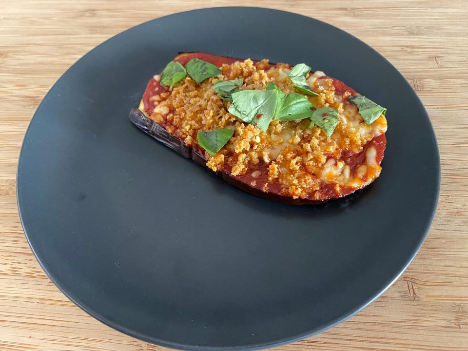 Eggplant Parmesan topped with basil on a gray plate.