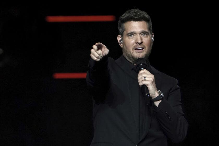 Michael Bublé wearing a black suit points from onstage while holding a microphone to his hand