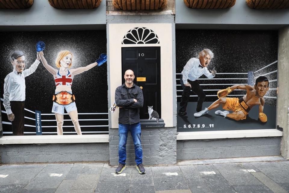 Artist Ciaran Gallagher beside his new mural depicting Liz Truss being declared a winner by Jacob Rees-Mogg after beating Rishi Sunak (Peter Morrison/PA) (PA Wire)