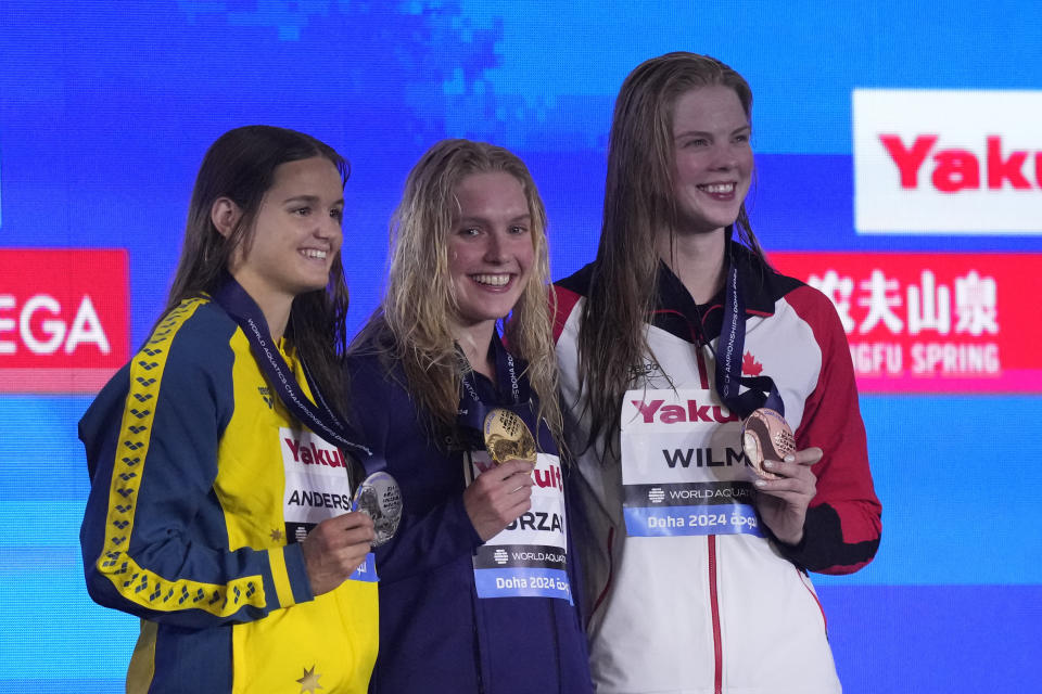 Gold medalist Claire Curzan of the United States, center, silver medalistIona Anderson of Australia and bronze medalist Ingrid Wilm of Canada pose for a photo during the medal ceremony for the women's 100-meter backstroke final at the World Aquatics Championships in Doha, Qatar, Tuesday, Feb. 13, 2024. (AP Photo/Lee Jin-man)