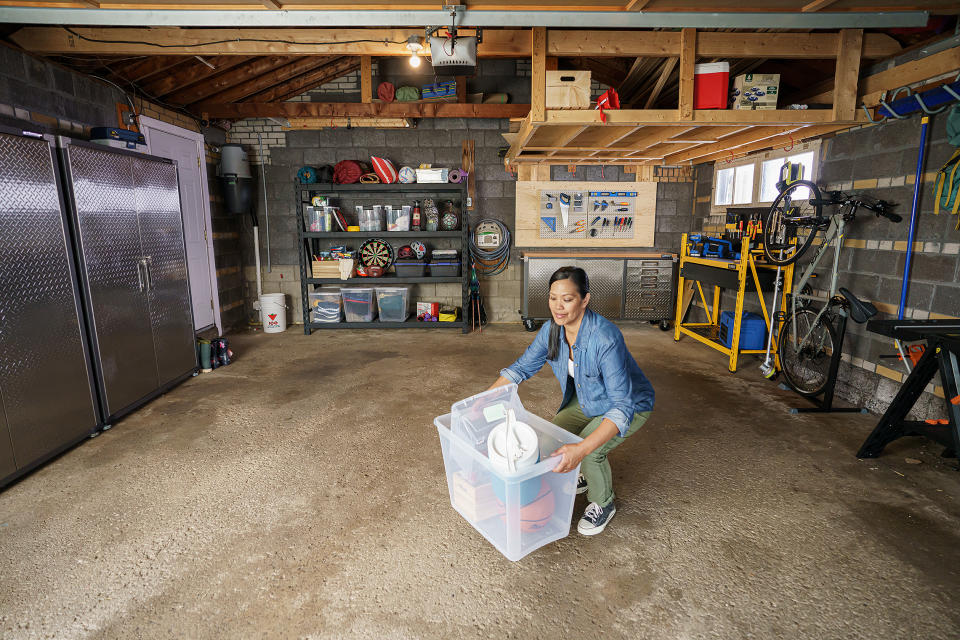Woman picking up a clear storage bin in an organized garage