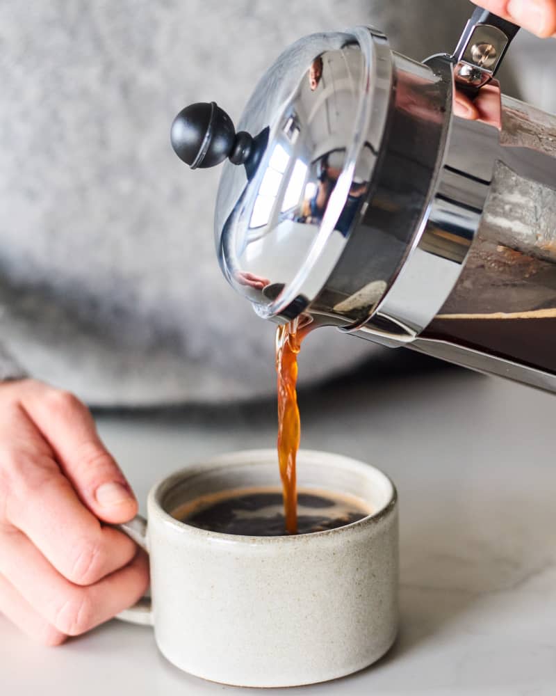 someone pouring coffee into a ceramic mug from a french press