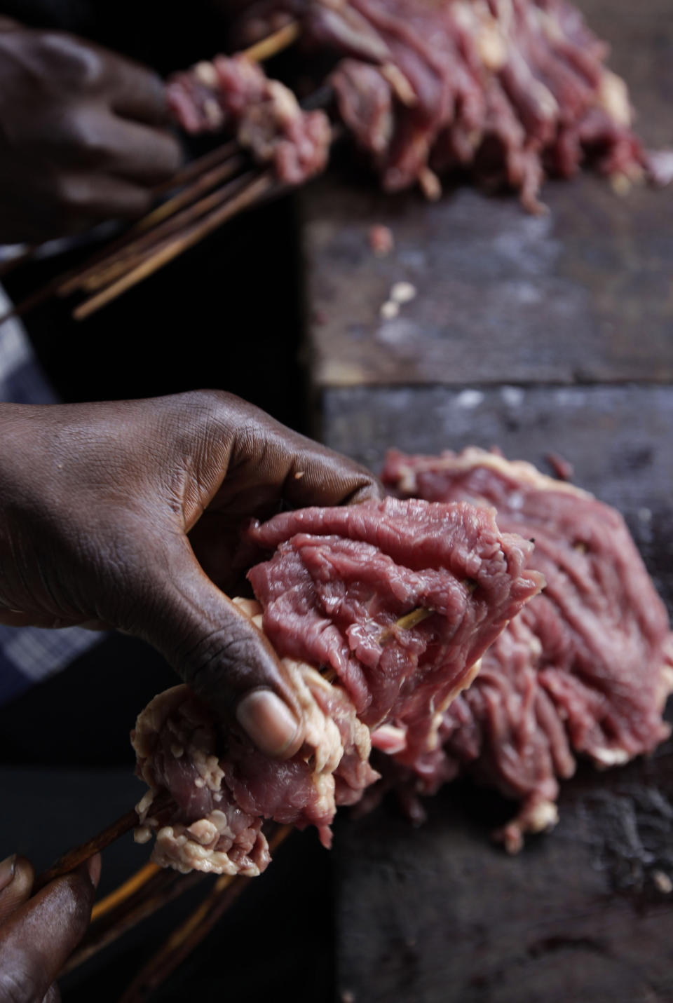 In this photo taken on Saturday, Oct. 20, 2012, men insert meat into sticks to prepare suya in Lagos, Nigeria. As night falls across Nigeria, men fan the flames of charcoal grills by candlelight or under naked light bulbs, the smoke rising in the air with the smell of spices and cooking meat. Despite the sometimes intense diversity of faith and ethnicity in this nation of 160 million people, that thinly sliced meat called suya, is eaten everywhere. (AP Photo/Sunday Alamba)