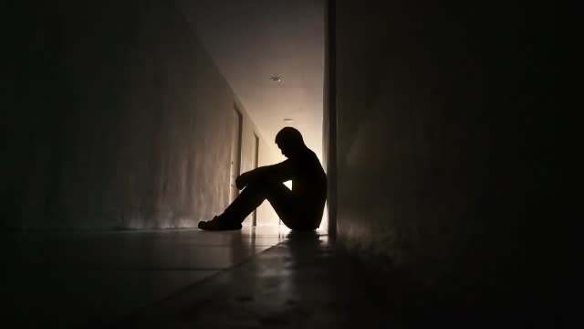 Silhouette of person sitting with head down against a wall