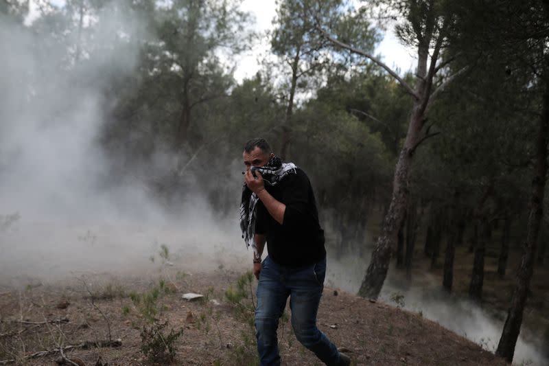 A man covers his face to protect himself from tear gas as demonstrators, who oppose the building of a new closed migrant detention centre clash with riot police, in the area of Diavolorema on the island of Lesbos