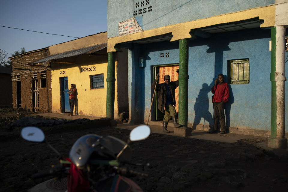 In this Sept. 4, 2019 photo, residents stand outside buildings as the sun rises in Kinigi, Rwanda. In 2005, the government adopted a model to steer 5% of tourism revenue from Volcanoes National Park to build infrastructure in surrounding villages, including schools and health clinics. Two years ago, the share was raised to 10%. (AP Photo/Felipe Dana)