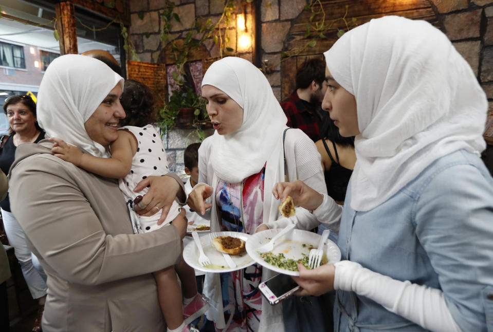 In this July 12, 2019, photo, Fatima Kwara, left, wife of Syrian refugee chef and co-owner Diaa Alhanoun, holds the couple's young daughter Masa, while chatting with her sister, Aminah Kwara, center, and daughter Ragad, in New York, at the opening of "Sakib" in Brooklyn's trendy Williamsburg neighborhood. Virtually all of Alhanoun's friends, colleagues and extended family attended the opening, as well as passers-by, who were welcomed into the restaurant and ate for free, courtesy of the owners. (AP Photo/Kathy Willens)