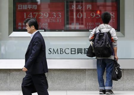 A man looks at electronic boards showing Japan's Nikkei average (L) and the exchange rate between the Japanese yen and the U.S. dollar outside a brokerage in Tokyo May 27, 2014. REUTERS/Toru Hanai