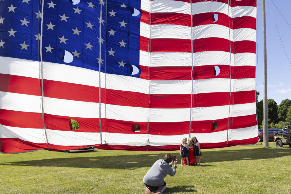 Brook Nugent poses with her twin daughters Maisie, left, and Sabrina, right, in front of a giant flag on display outside the National Flag Foundation in Waubeka, Wis., on June 9, 2024. Old Glory is venerated annually in Waubeka, the small town that lays claim to the first Flag Day. (AP Photo/Teresa Crawford)