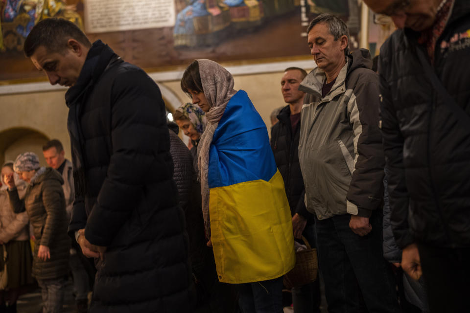 Orthodox Christian worshiper covered with the Ukrainian flag attends an Easter Sunday mass in Kyiv, Sunday, April 16, 2023. (AP Photo/Bernat Armangue)